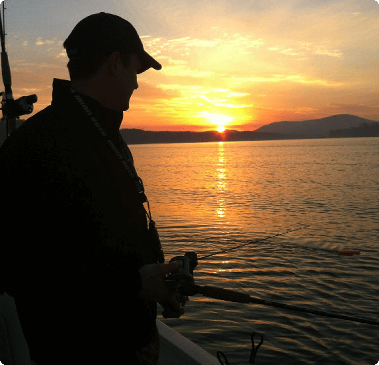image (8) Silhouette of a person fishing on a boat at sunset, with calm water and distant hills under a colorful sky.